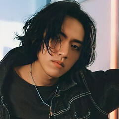 Kpop artist DPR Ian, A South Korean man with medium length dark hair and dark eyes, leans against the wall while staring intently into the camera.